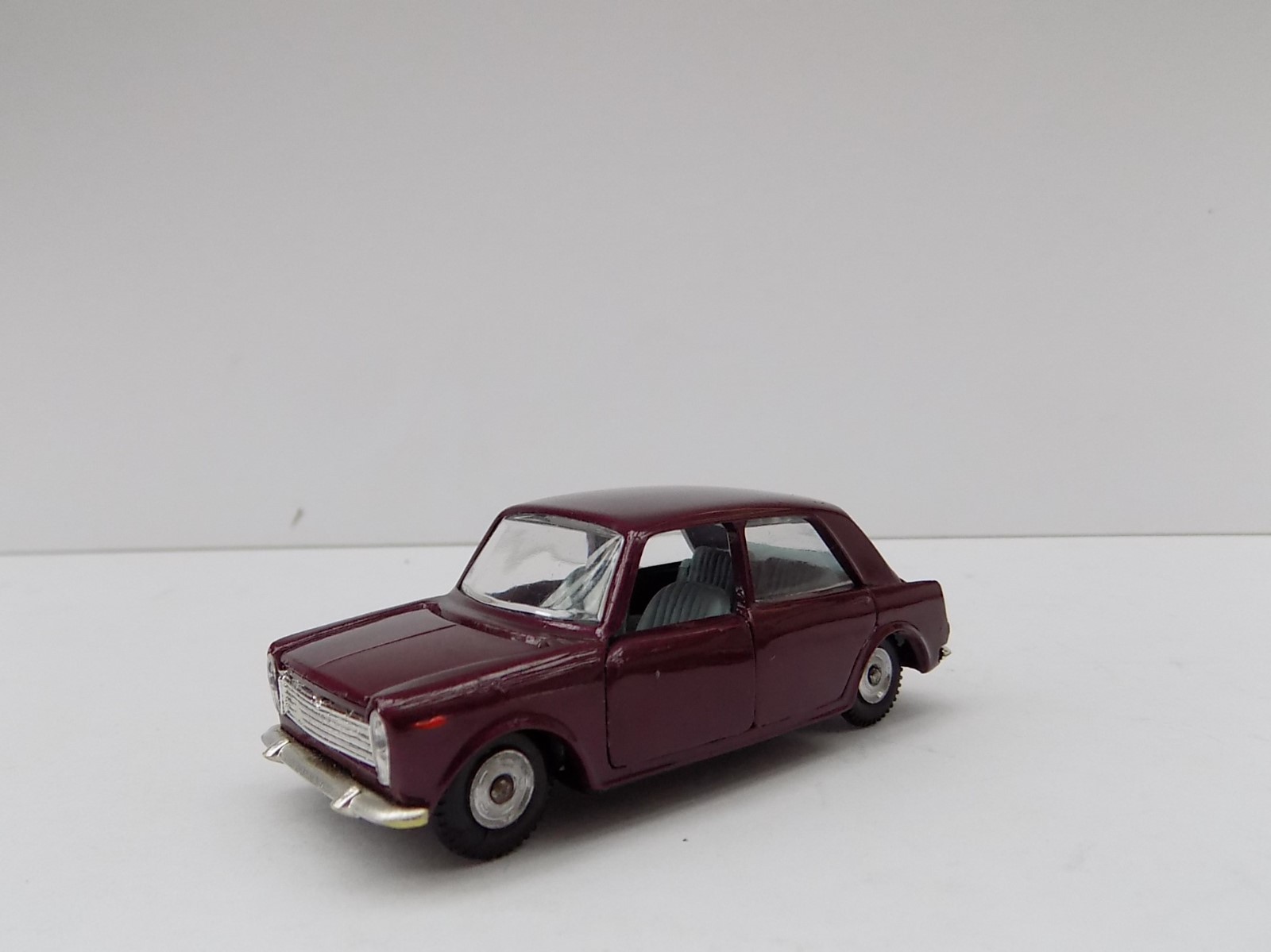 Peinture gouache mate d'une maquette de voiture de collection rouge foncé sur un fond gris clair, évoquant le catalogue de modèles réduits.