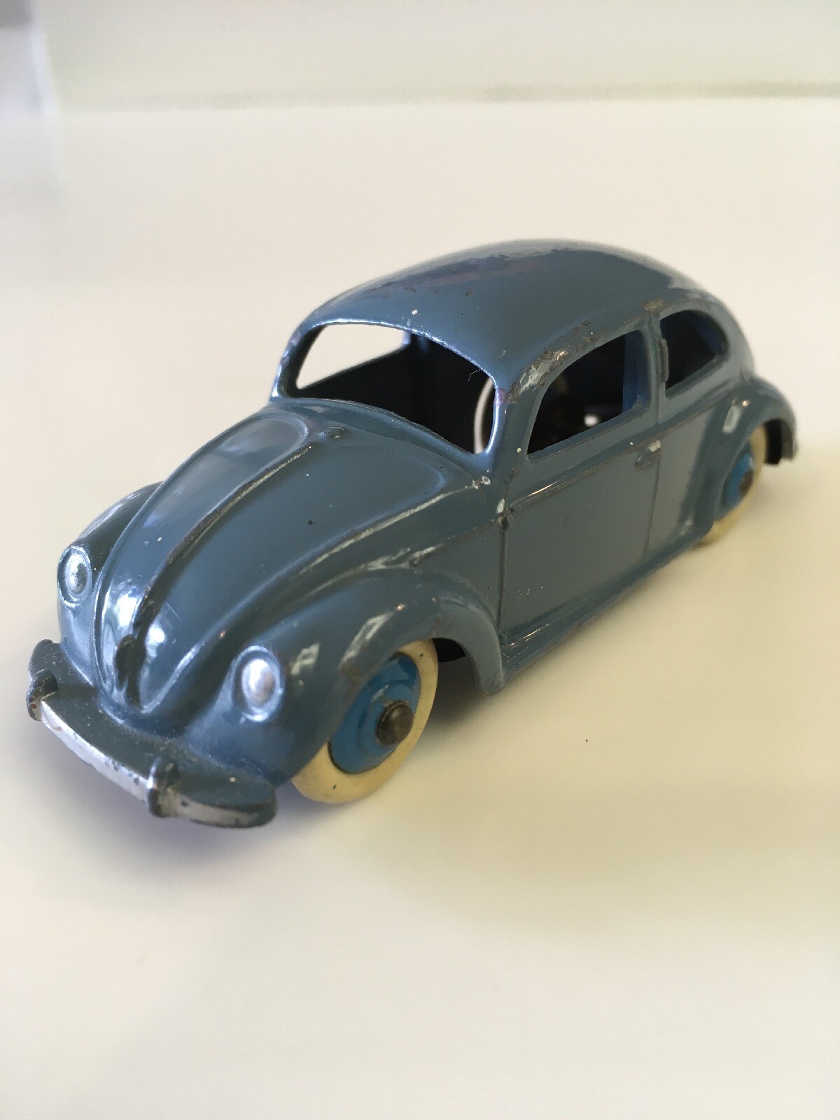 Voiture miniature bleu-gris avec roues crème, sur fond clair uni